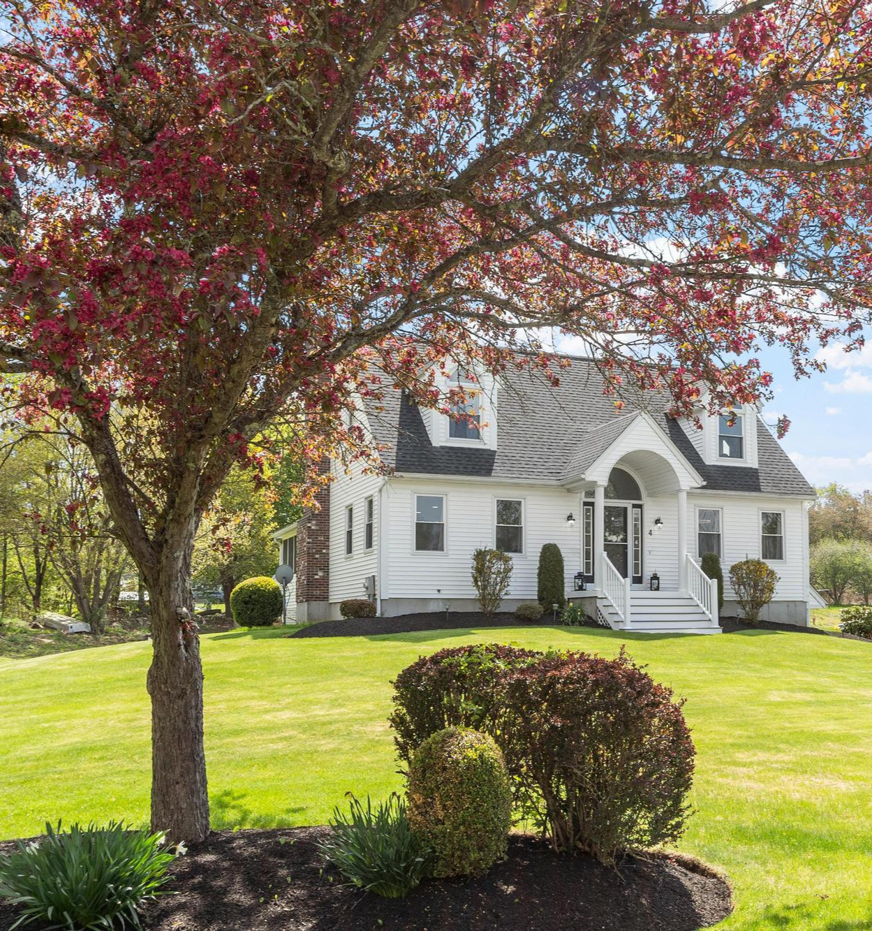 4 Ashton Lane, Sterling Massachusetts — a classic white New England Cape with twin arched dormers on a sunlit lawn